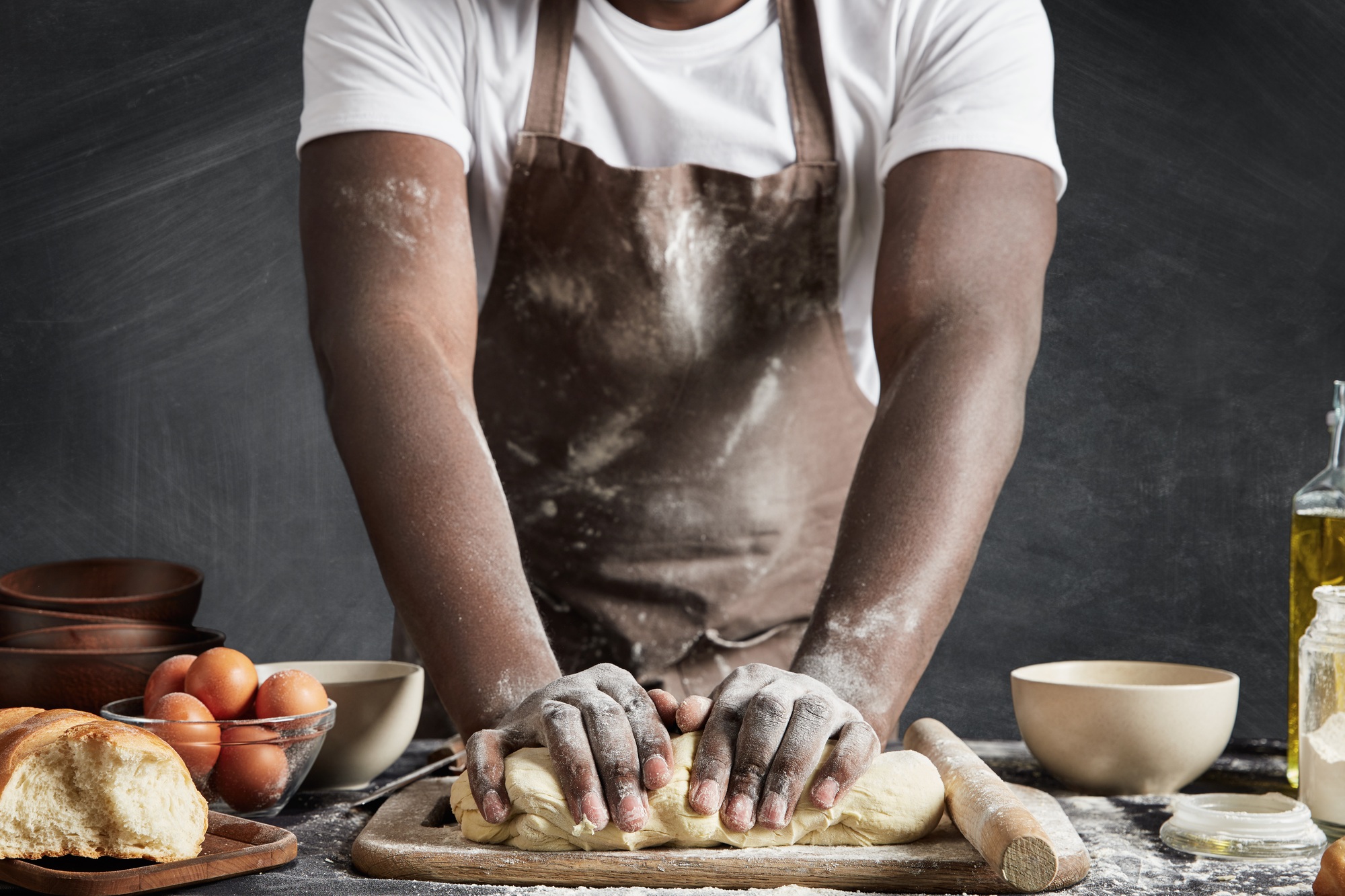 Cropped shot of dark skinned talented male cook kneads dough on wooden counter, going to bake delici